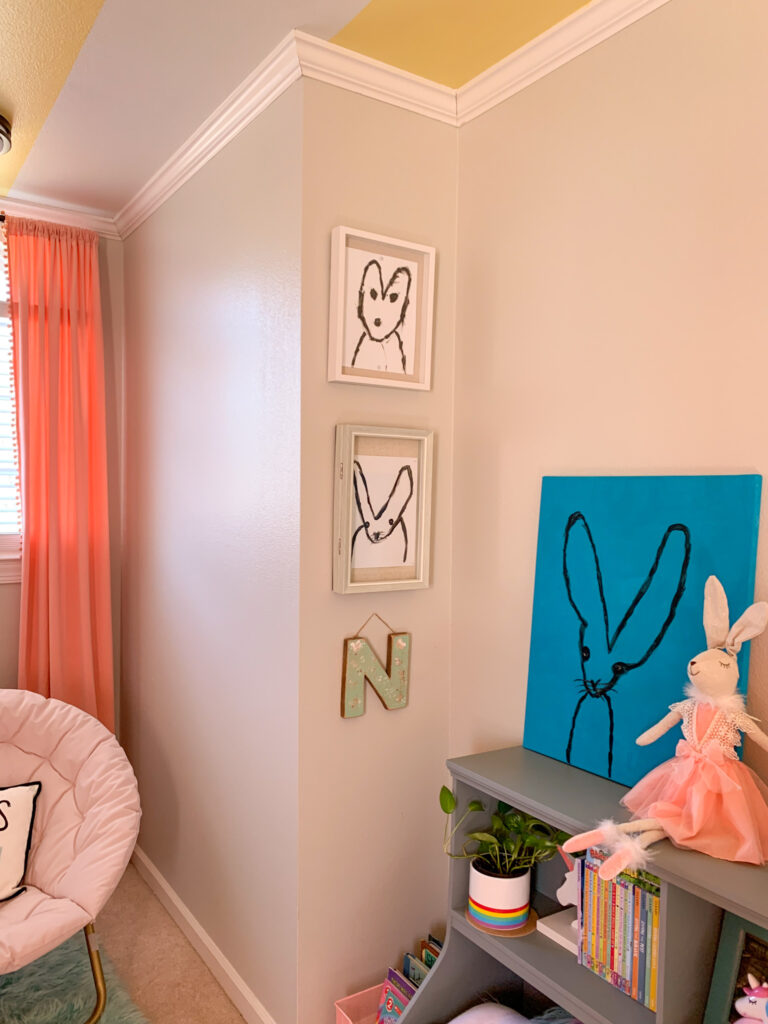 blue bunny painting with stuffed bunny on shelf and three framed bunnies drawings on the wall