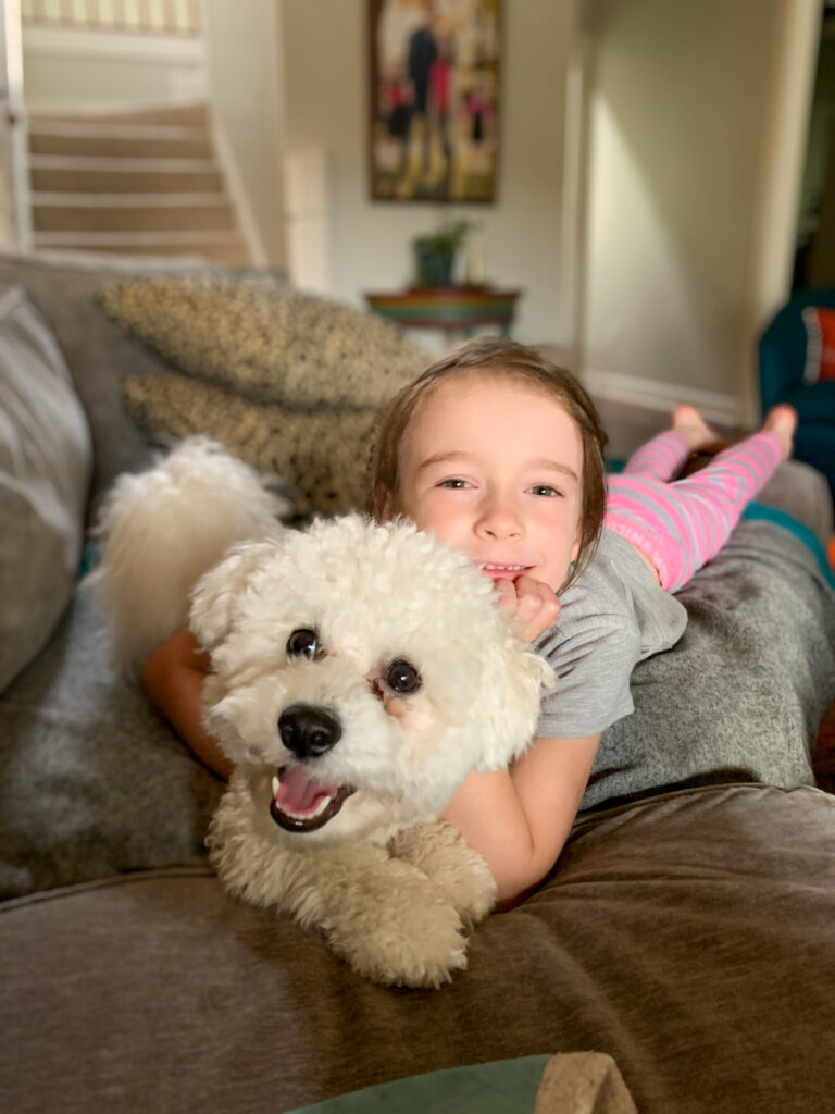 Bichon Frise and children blogger, Norah, cuddling on couch