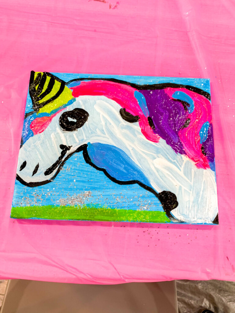 a finished canvas dries on top of a pink tablecloth