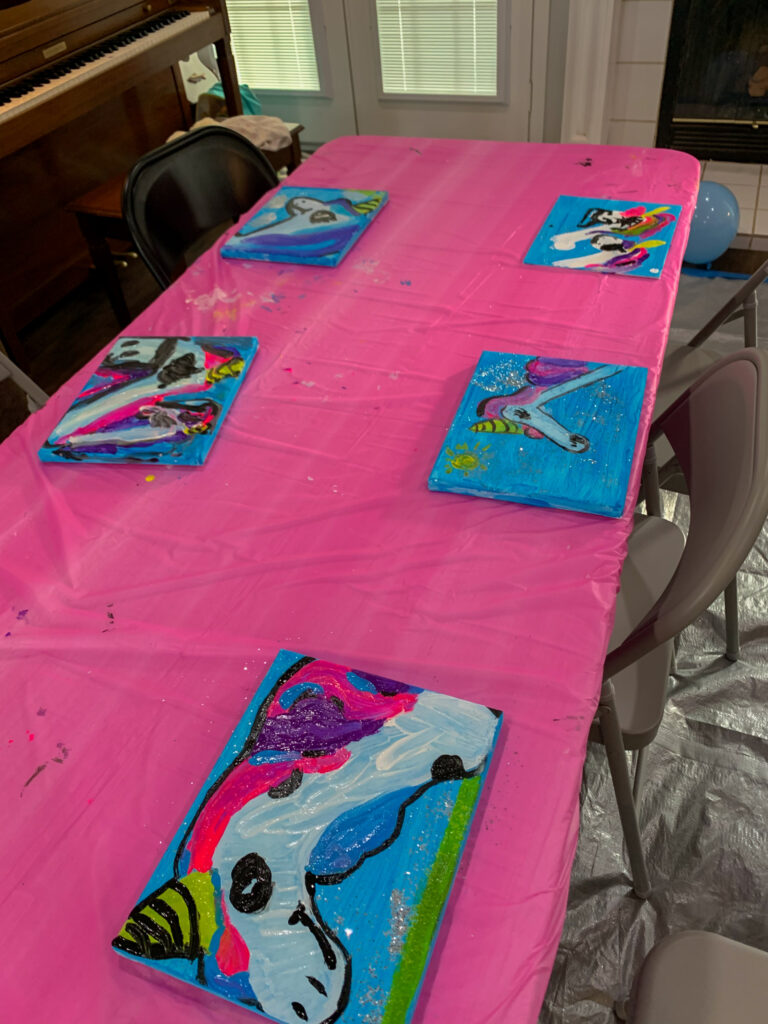 finished canvases from a unicorn paint party on a table with a pink tablecloth