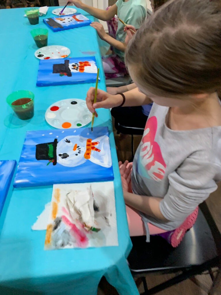 girl paints a snowman on canvas at a snowman paint night