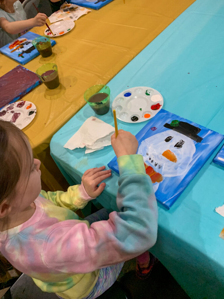 little girl painting arylics on canvas at a snowman paint night