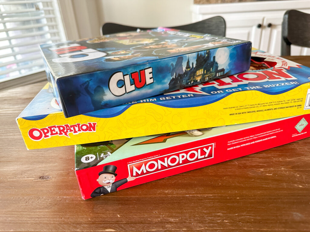 best board games for 8 year olds stacked on table - Clue, Operation and Monopoly