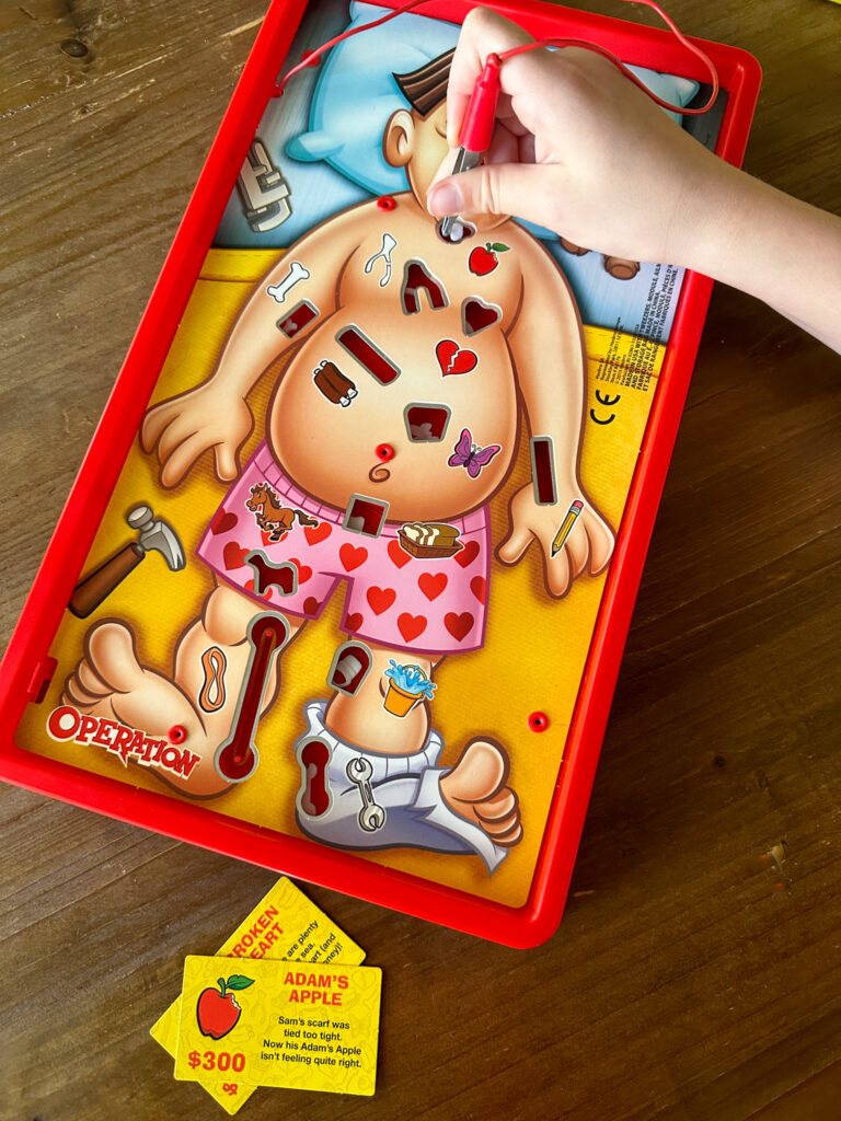child plays with Operation game as best board games for 8 year olds and challenge cards on table
