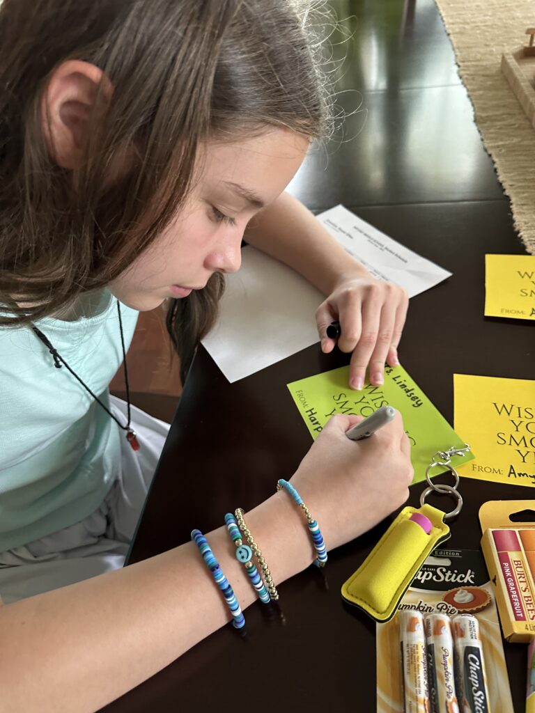 little girl writes her name on teacher gift tags for lip balm gift