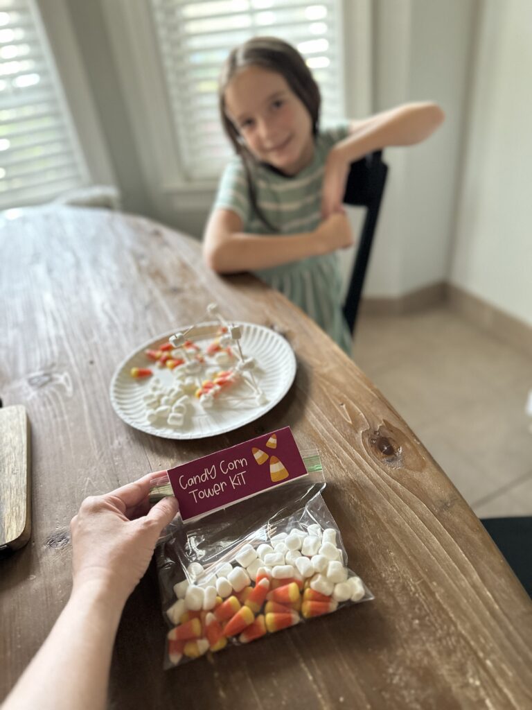 woman holds Halloween candy corn tower STEM kit at table in front of child