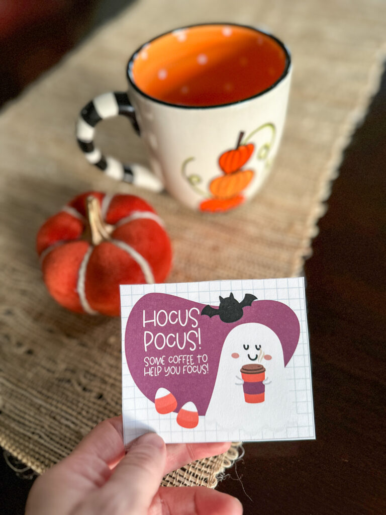 woman holds free printable Halloween teacher gift tab in hand in front of gift items on table