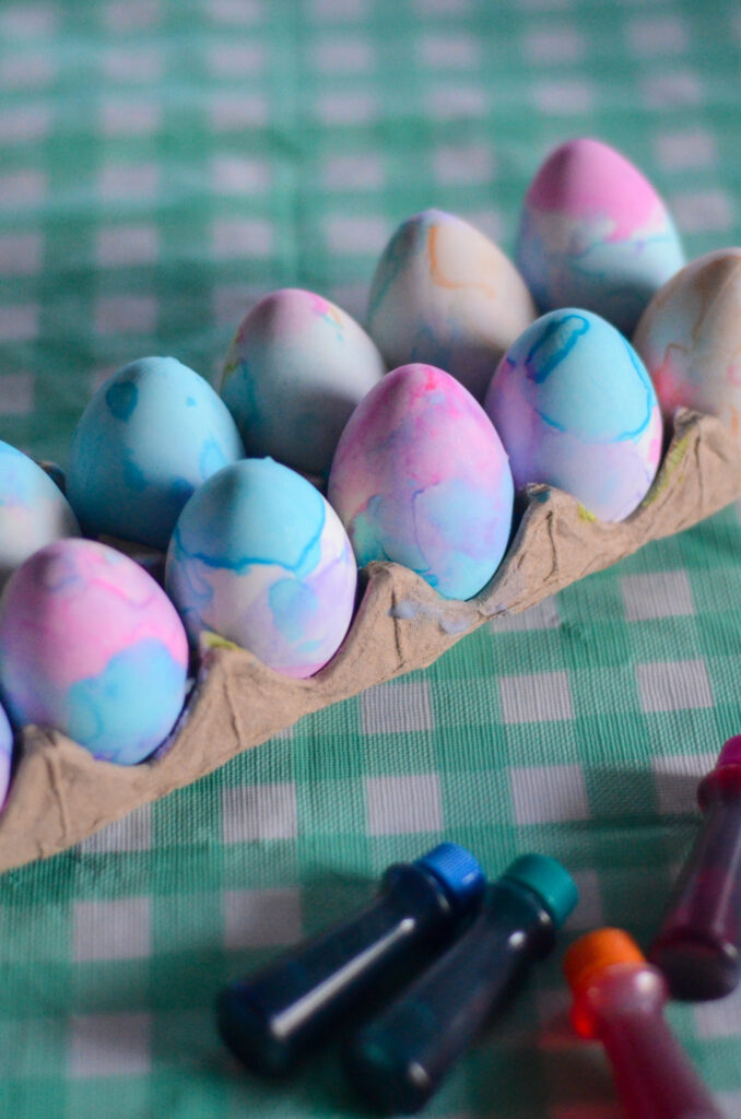 food coloring Easter eggs with whipped cream in paper carton with neon food coloring bottles at side