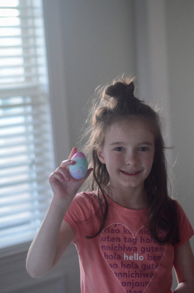 little girl holds a marbled food color Easter egg with Cool Whip in hand