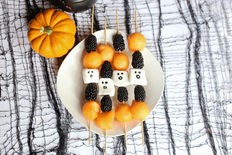fruit ghost skewers on spiderweb backdrop with pumpkin to side