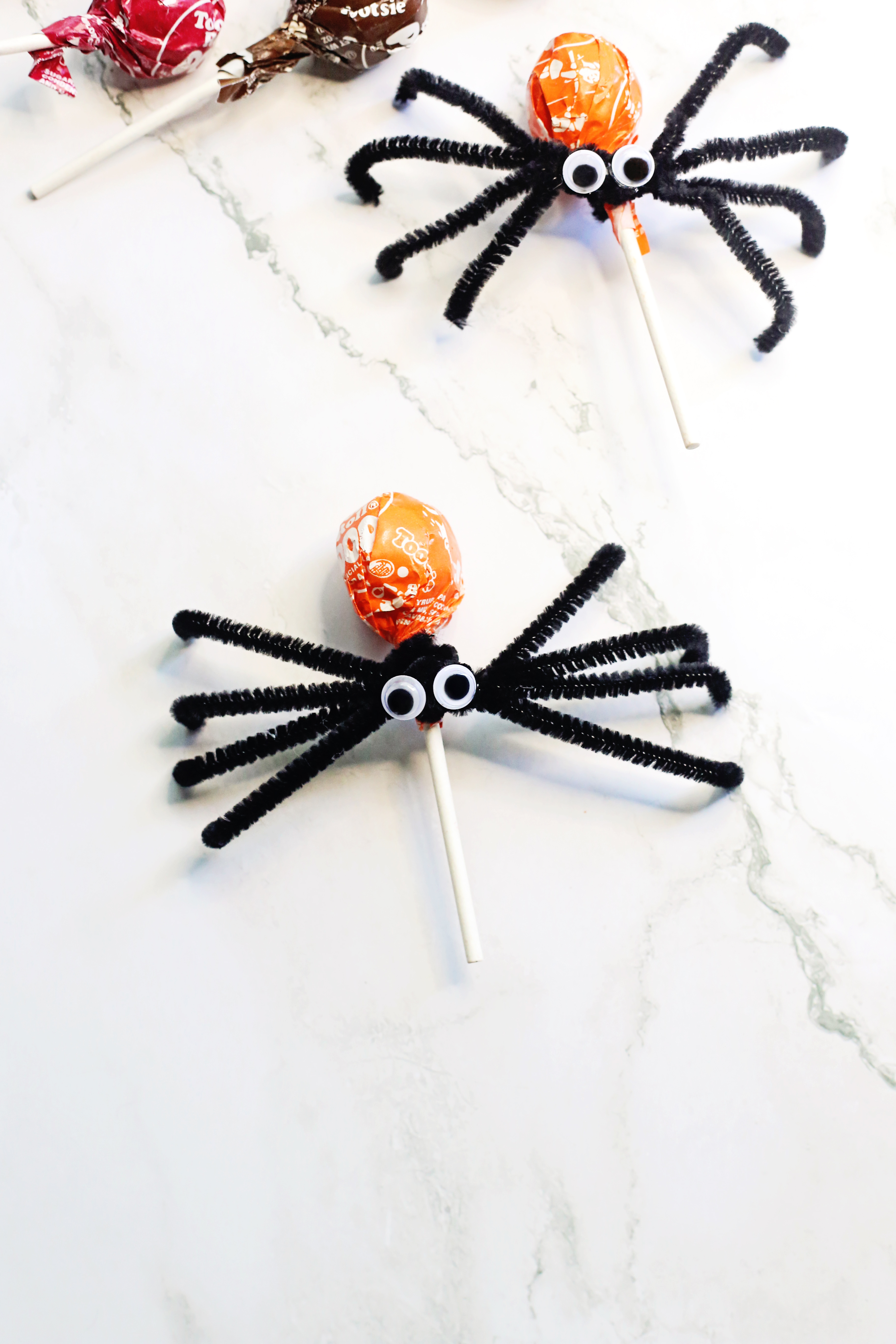 two Halloween spider lollipops with pipe cleaner and Tootsie Pops on table