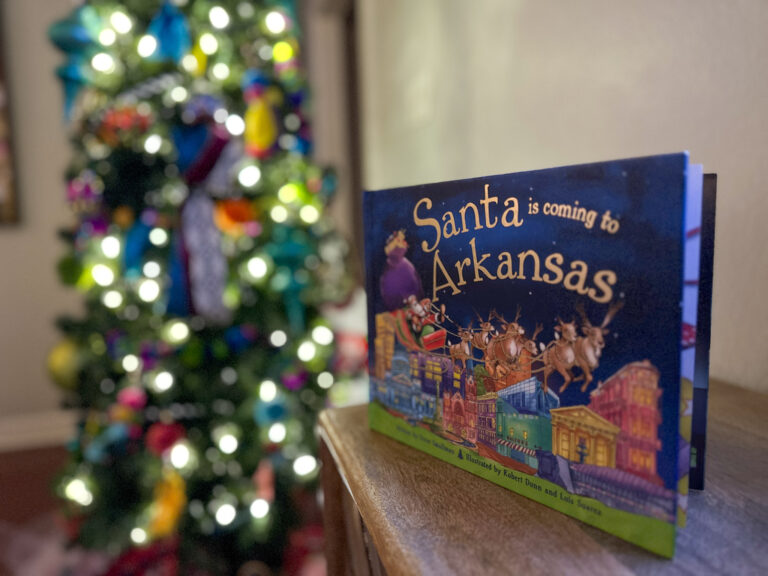 Christmas Around the World book collection with Santa is Coming to Arkansas on table in front of lit tree
