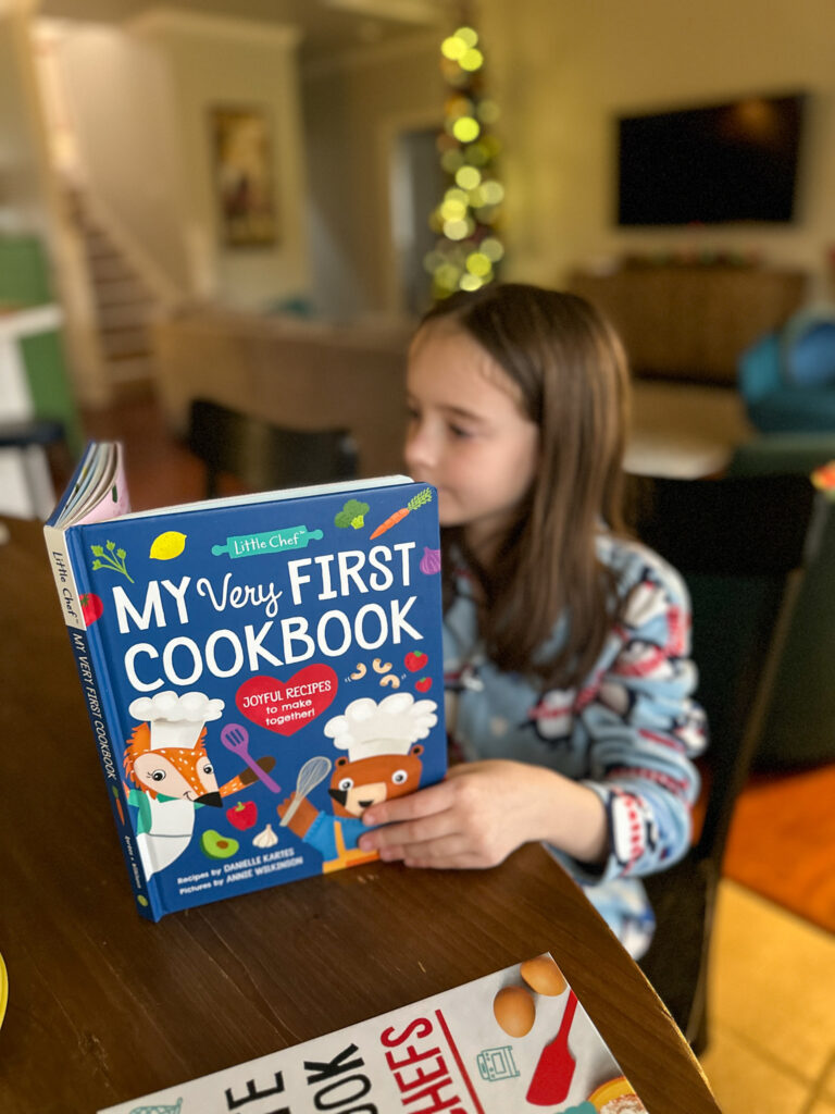 little girl with cooking gifts for kids who love to cook - her first cookbook