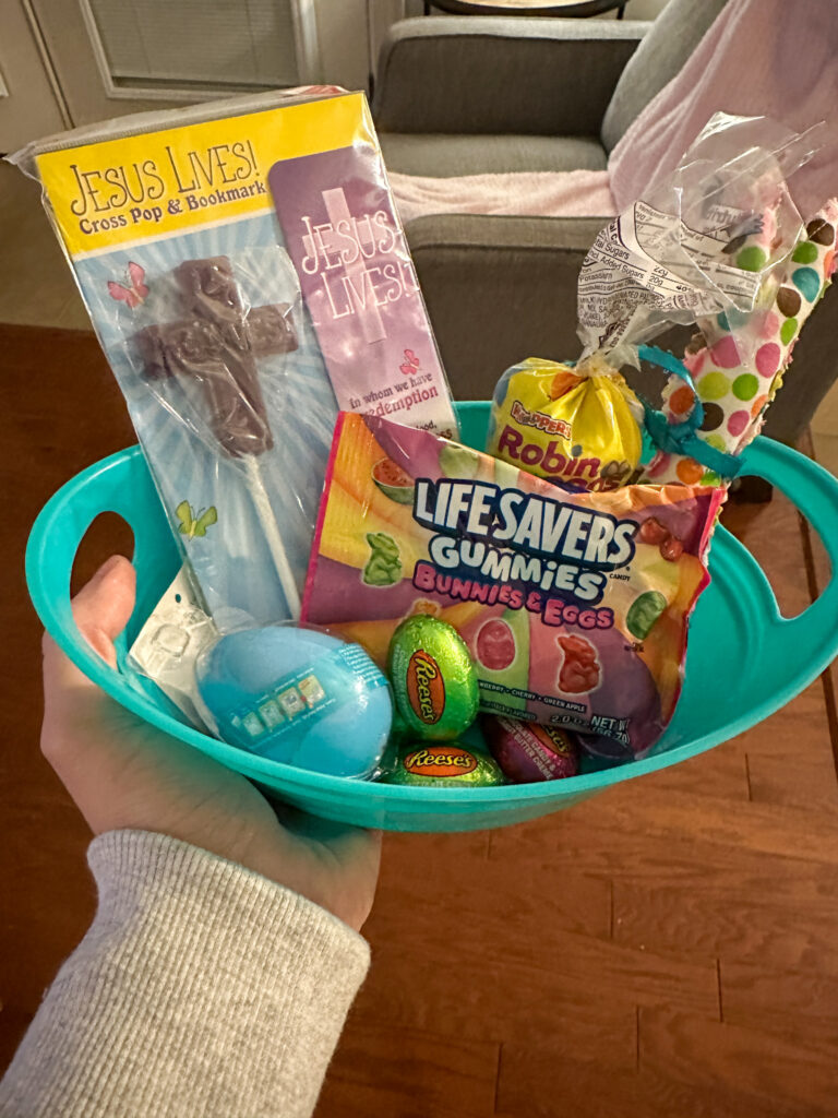 Bunny Blessings box gift ideas in a blue bin in woman's hand, including a Jesus Lives cross pop and bookmark