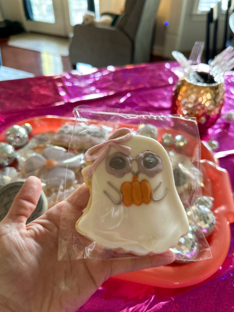 woman holds ghost cookie with pumpkin and disco balls at back for a Halloween Let's Glow, Ghouls theme for teens